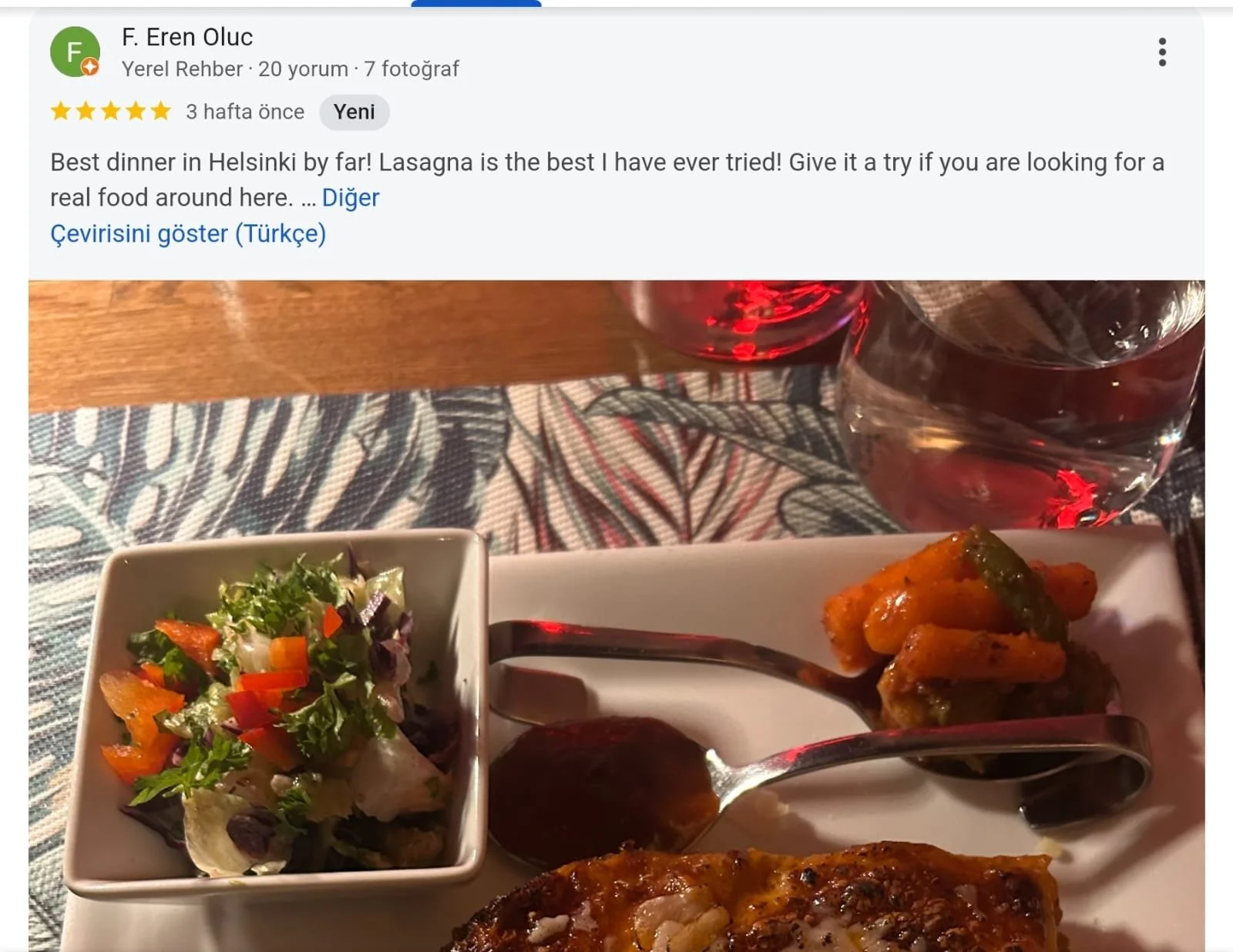 Plate of food with a small bowl of salad, two spoonfuls of curry or stew, and a piece of baked chicken with herbs. Two glasses of red wine in the background.